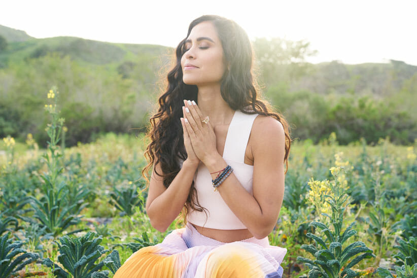 Kimberly Snyder in a field of flowers with hands in prayer position