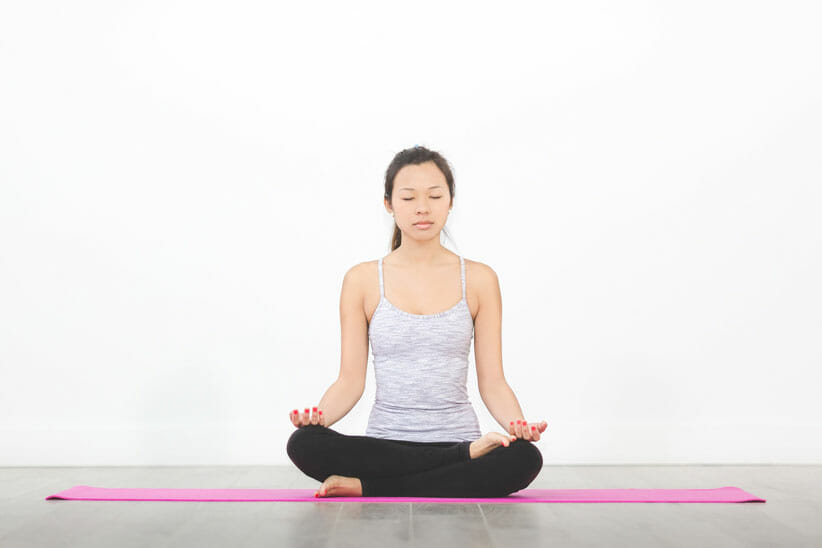 Woman on pink yoga mat in meditation pose set up to deepen your practice 
